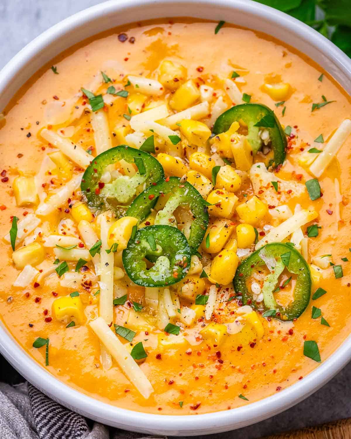 A white bowl of Mexican Street Corn Soup topped with cheese and jalapeno.
