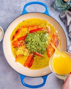 broth being added over the pesto and peppers in a pan.