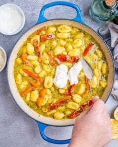 adding yogurt to the pesto gnocchi in the pan.