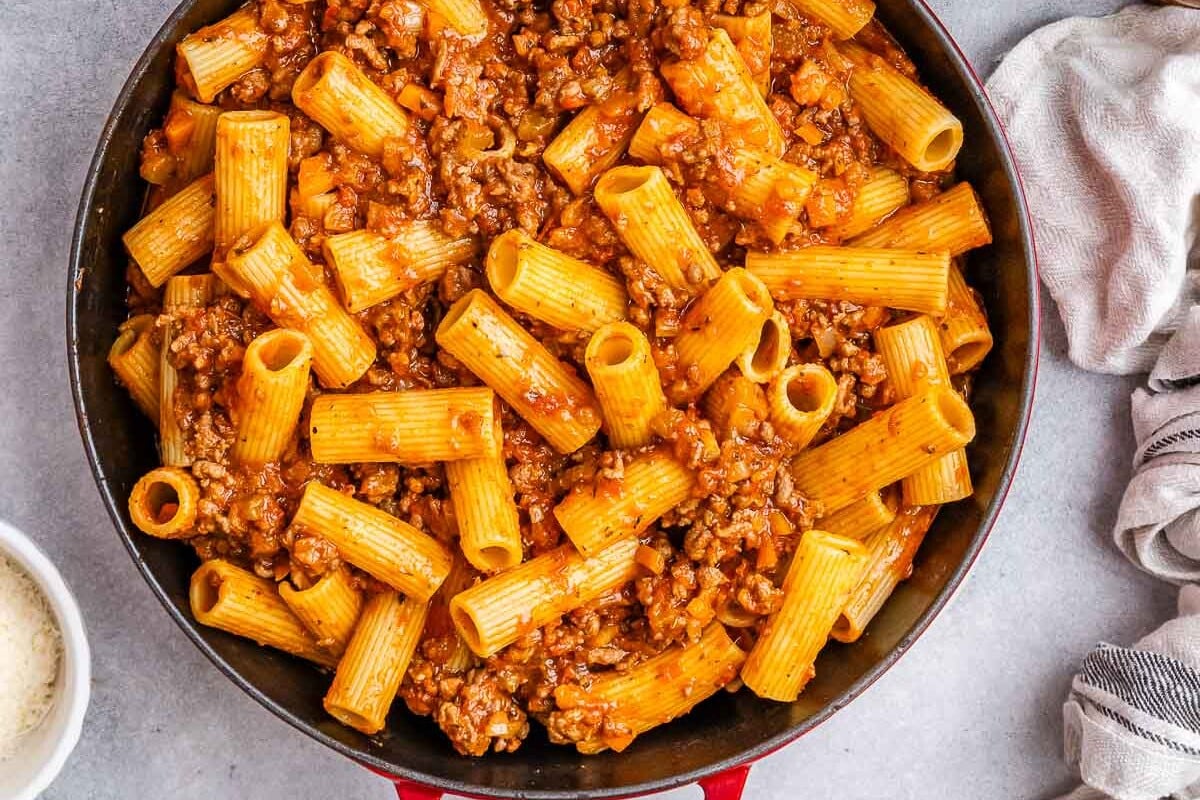 rigatoni pasta with meat sauce in a red skillet.