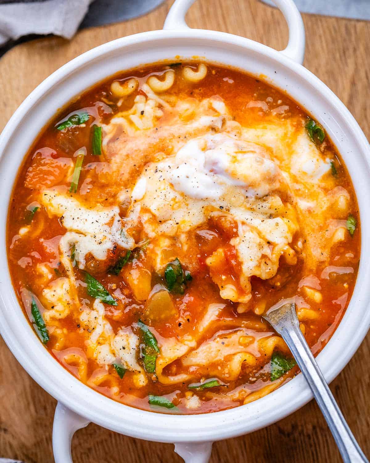 A white bowl of vegetarian lasagna soup topped with mozzarella and parmesan.