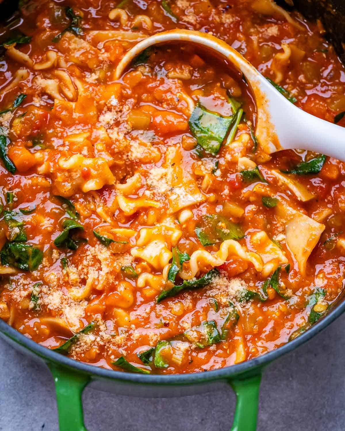 A green pot with vegetarian lasagna soup and white ladle.