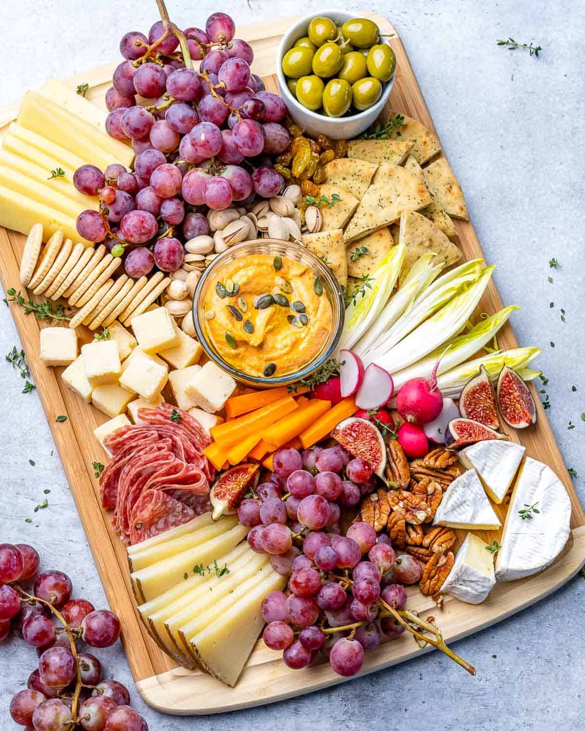 a wooden platter with nuts, fruits, and cheese.
