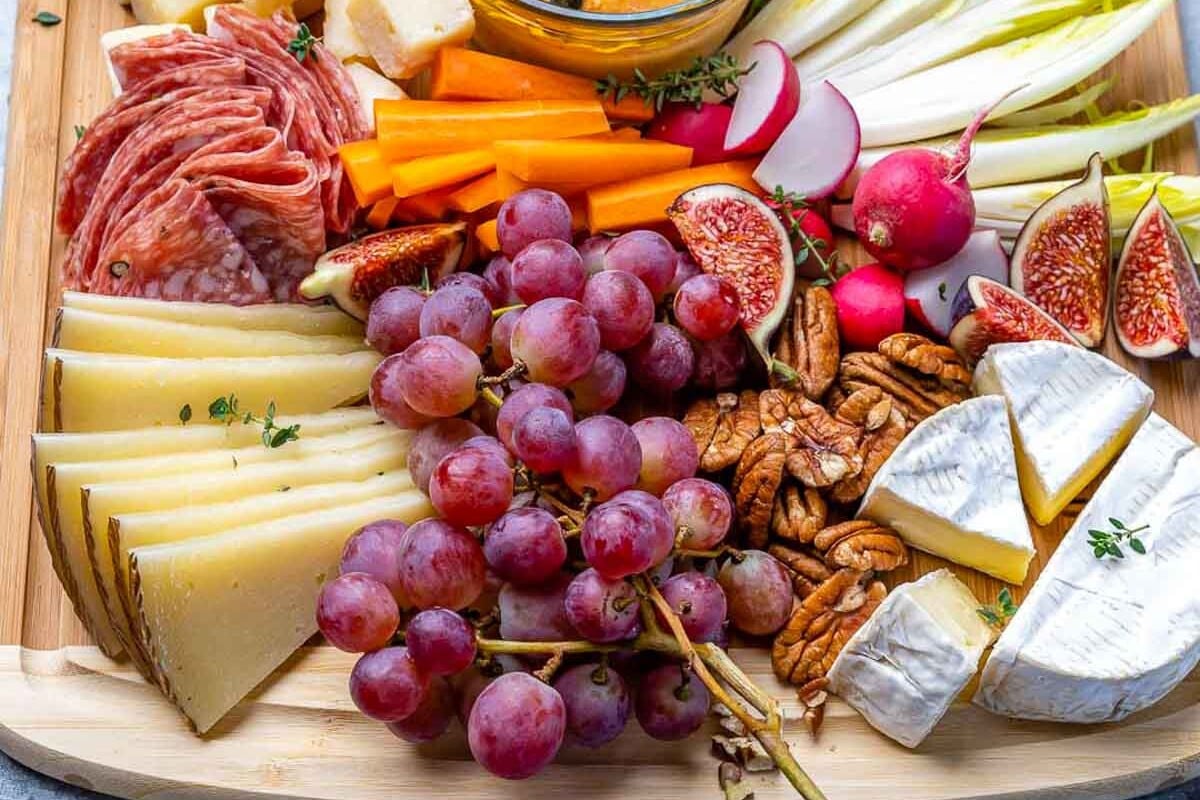 cheese, fruits, and nuts on a cutting board.