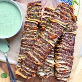 tortilla kebabs on a cutting board next to a small bowl of cilantro cream sauce dip.