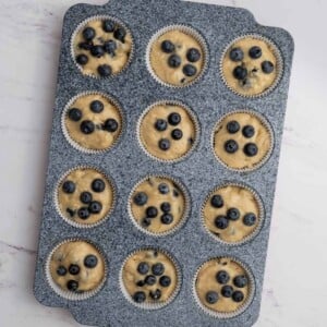 batter added to muffin pan and topped with blueberries.