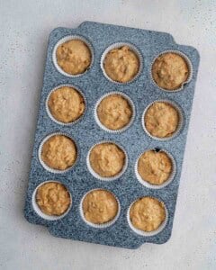 batter adding into muffin cups in a pan.