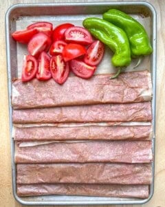 doner rolled meat placed on parchment paper with peppers and tomatoes.