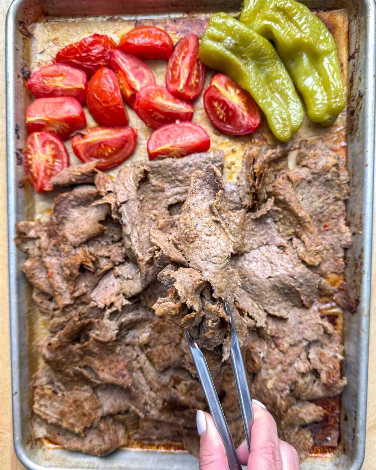 tongs grabbing some doner kebab from the pan.