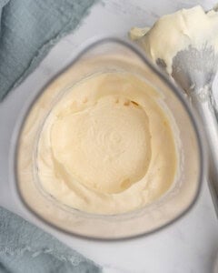 Close-up of thick, creamy homemade mayonnaise in a tall glass mixer, showing the smooth, emulsified texture after blending, with an immersion blender lying next to it with mayonnaise on the end.