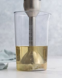 Immersion blender held steady at the bottom of the jar, with the base of the mixture starting to thicken into creamy mayonnaise.