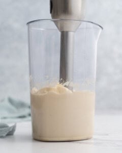 Fully blended thick, creamy homemade mayonnaise in a tall glass jar with an immersion blender in it, ready to be transferred.