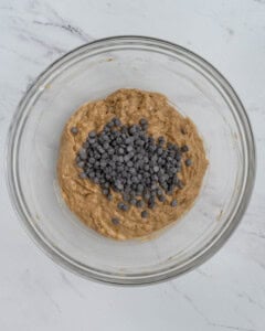 Chocolate chips are added to the batter in a bowl.
