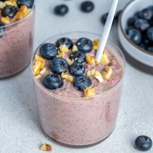 a cup with blueberry oatmeal topped with fresh blueberries and walnuts.