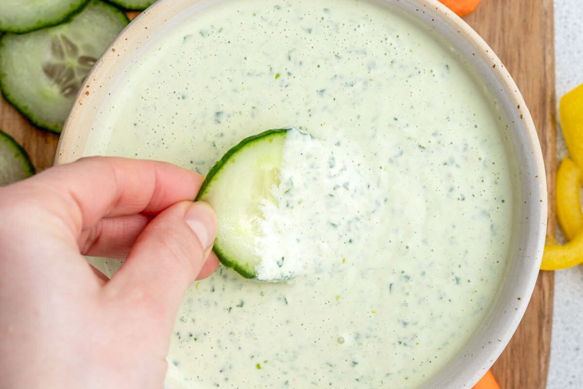 hand holding a slice of cucumber and dipping it in the dressing.