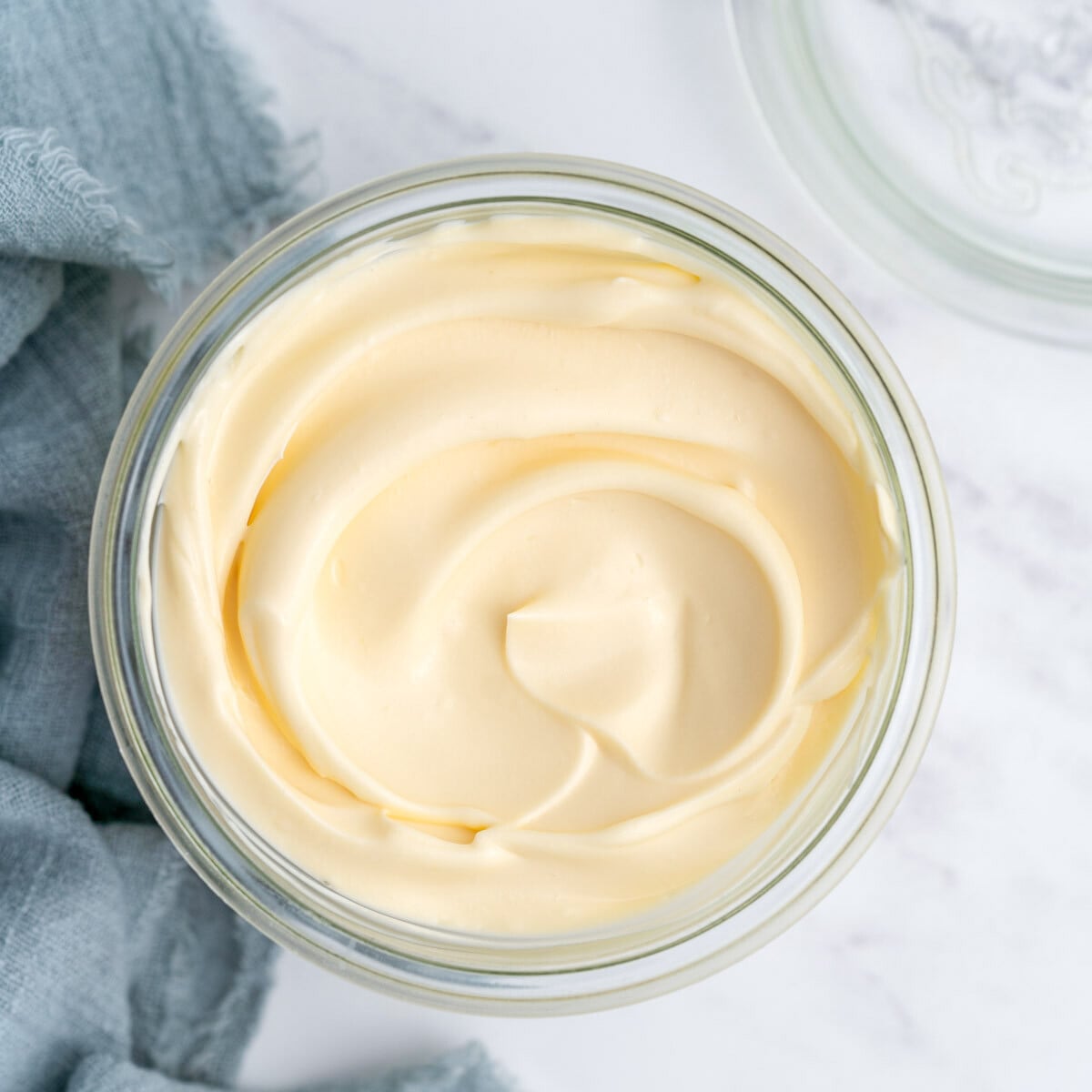 Completed homemade mayonnaise in an open glass jar, showing its glossy, pale yellow surface and creamy texture.