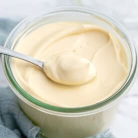 Spoon lifting a generous dollop of creamy homemade mayonnaise from a jar.