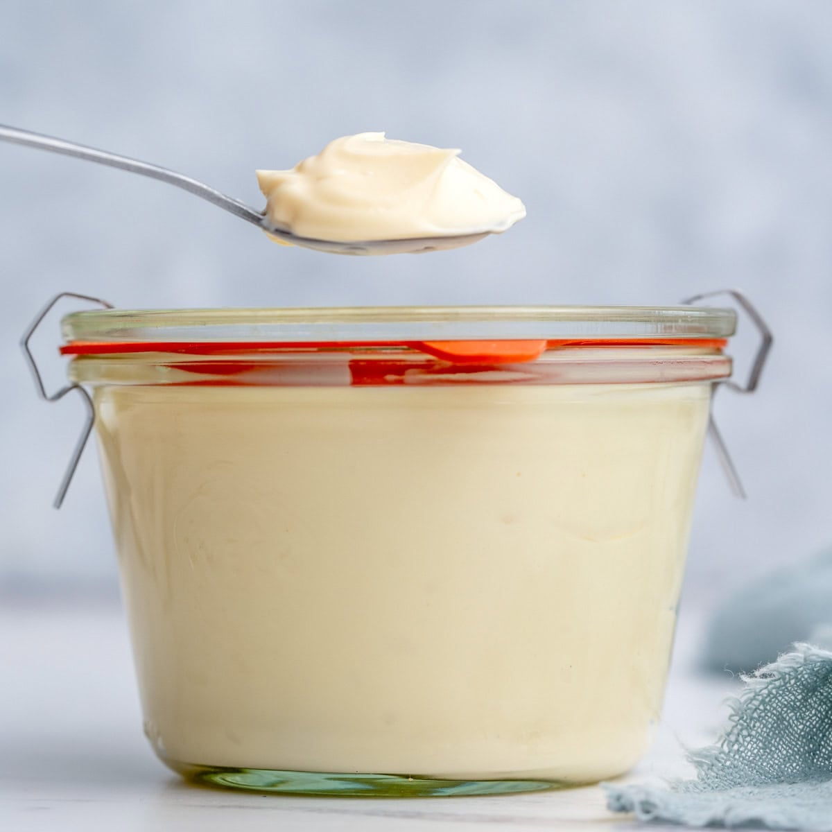 Finished homemade mayonnaise stored in a small glass jar with a red-handled lid, sealed and ready for refrigeration.