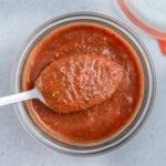 a jar full of pizza sauce with a spoonful of sauce over the jar.