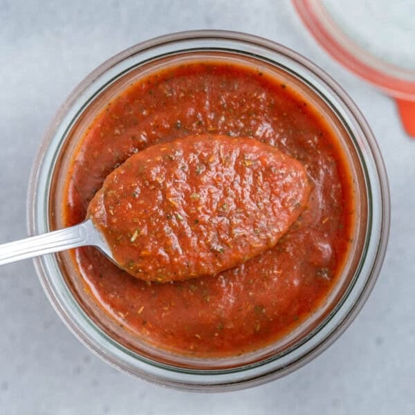 a jar full of pizza sauce with a spoonful of sauce over the jar.