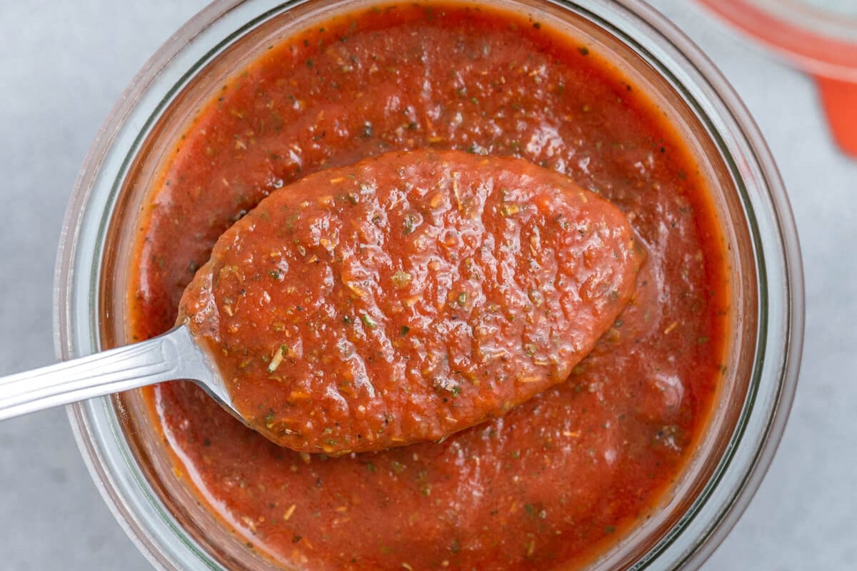 a spoonful of pizza sauce over a jar filled with pizza sauce.