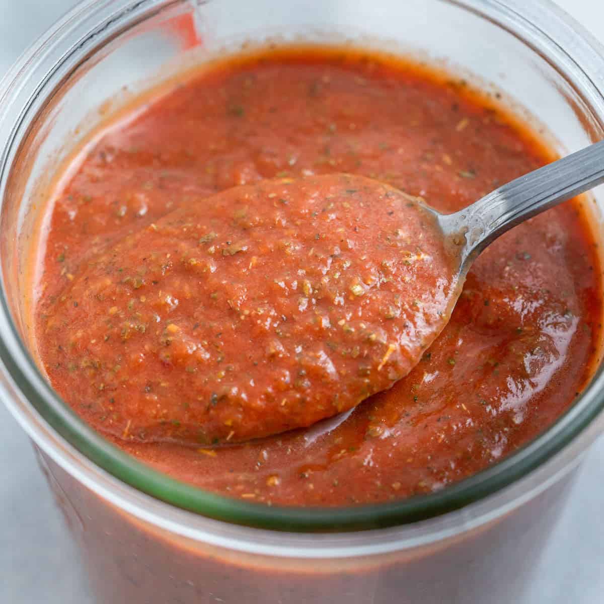A spoon scooping up homemade pizza sauce from a jar.