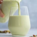 Pouring pistachio milk from a bottle into a cup.