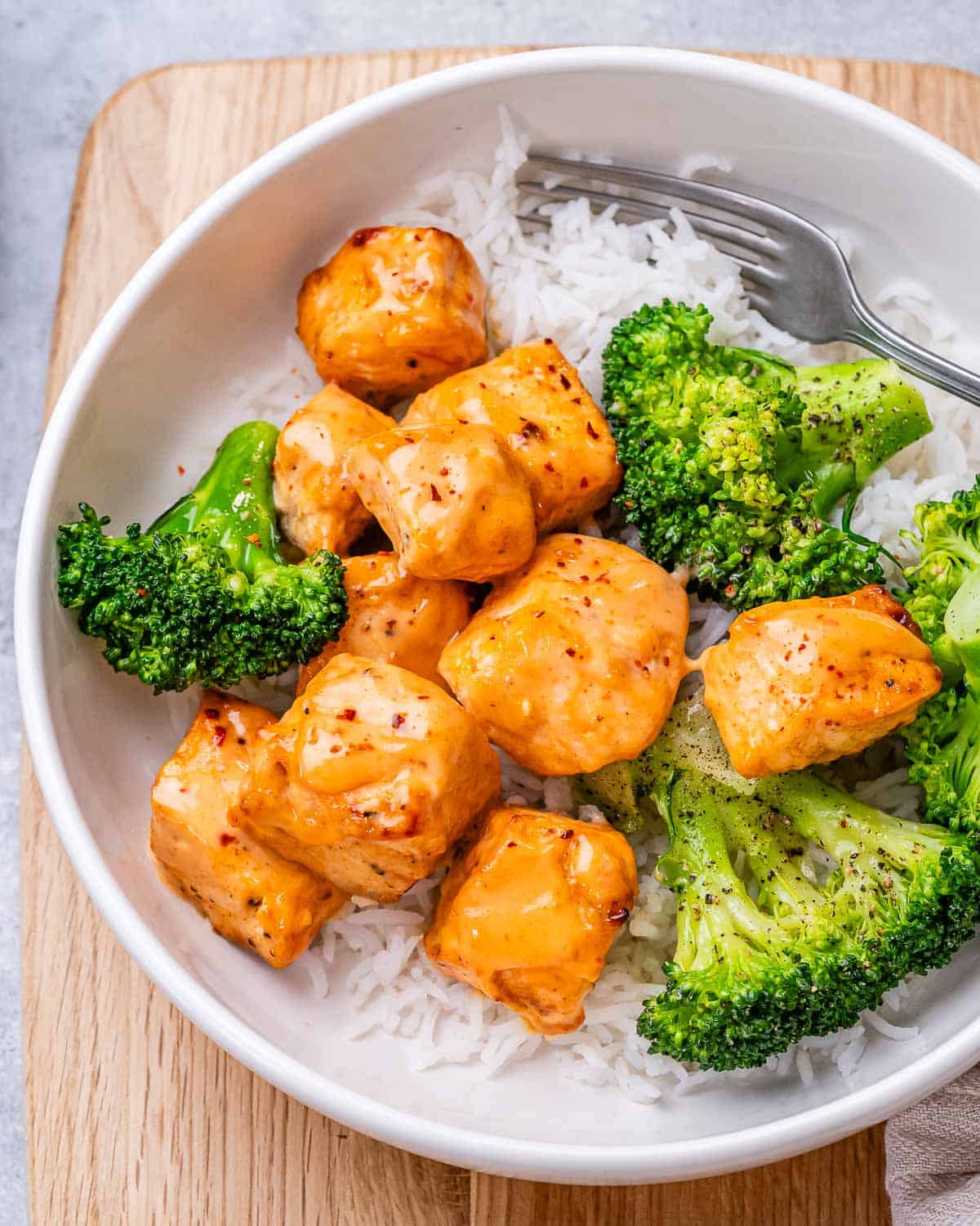 A white bowl with rice, bang bang salmon and broccoli.