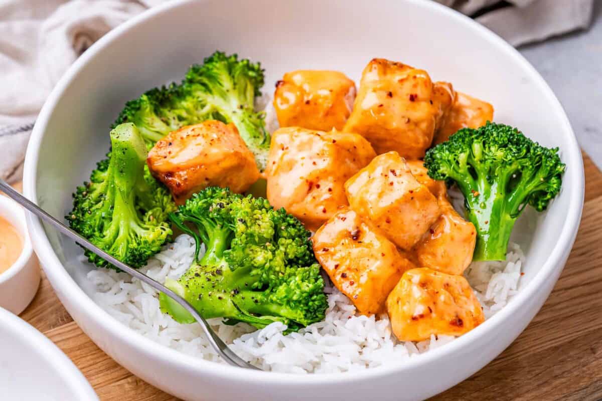 a bowl with rice topped with baked bang bang salmon and broccoli.