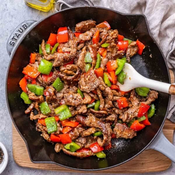 a skillet with black pepper beef made with green and red bell peppers, but white spoon in the skillet.