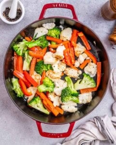 Top view of a red pan with cauliflower, broccoli, and red pepper being browned.