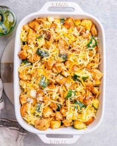 cheese sprinkled over chicken and zucchini in a baking dish.