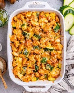 a white baking dish with baked chicken and zucchini bites topped with cheese.
