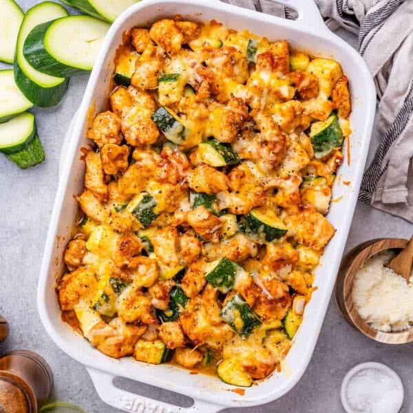 a white baking dish fillled with chicken and zucchini baked and topped with melted cheese.