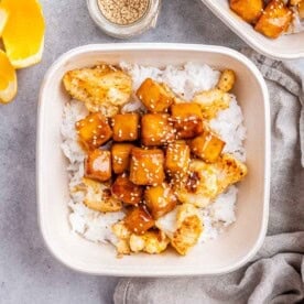 a meal prep bowl with crispy orange tofu served with roasted cauliflower over white rice.
