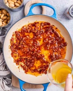 broth being added over the seared tomatoes and veggies in a skillet.