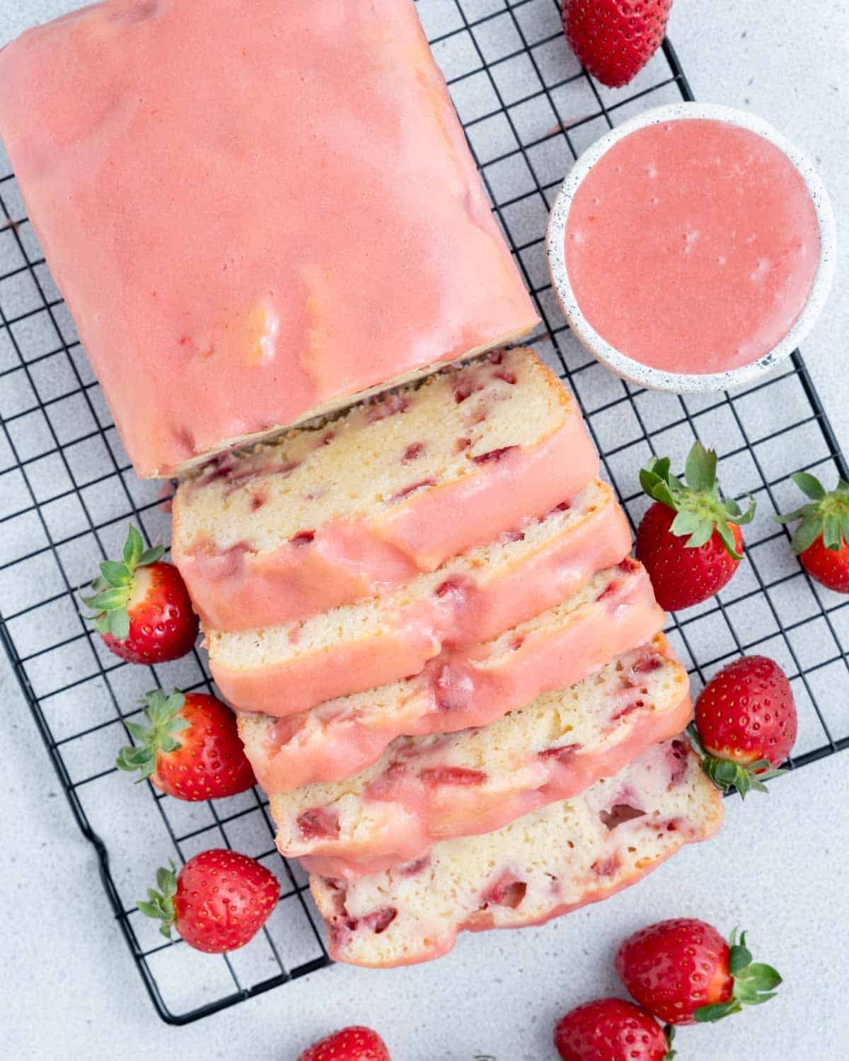 strawberry pound cake on a wire rack topped with strawberry glaze, with half of cake sliced.