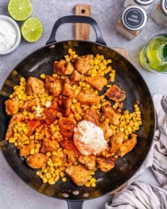 seasonings, sour cream, and mayo added to the chicken and corn in a pan.