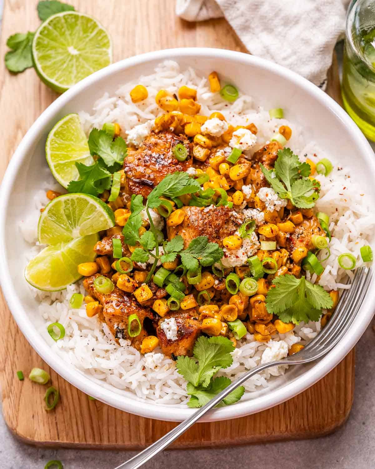 a round white bowl with rice topped with seared chicken breast chunks and street corn salad.
