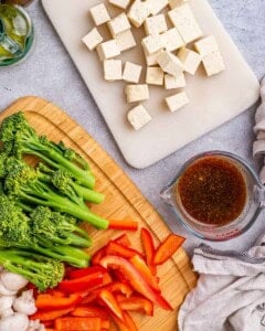 Tofu cut into uniform 1-inch cubes on a cutting board, next to prepared vegetables and soy sauce.