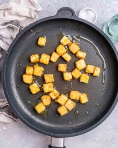 Tofu cubes frying in a hot non-stick pan with vegetable oil turning golden brown.