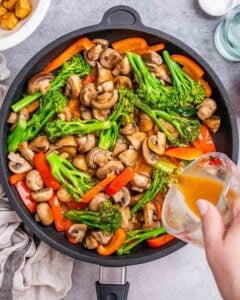Top view of frying pan with vegetables simmering, while the sauce is being poured in.
