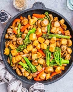 Top view of frying pan with vegetables and tofu cubes being fried together in stir fry sauce.