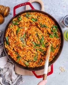 Large pot of orzo pasta coated in a rich tomato-balsamic sauce, swirled with wilted fresh spinach leaves and scattered sun-dried tomato pieces.