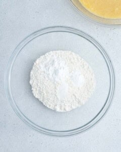 flour, baking powder, baking soda, and salt added to a clear bowl to be mixed.