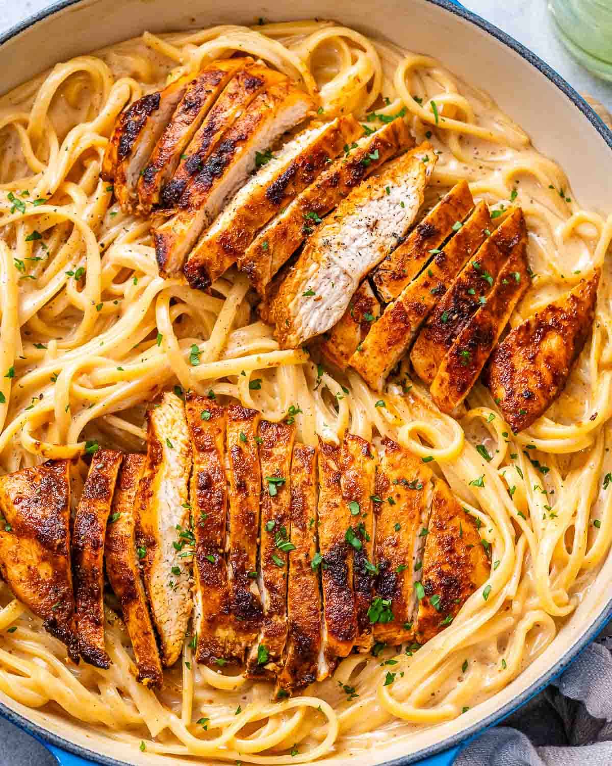 pasta in a skillet in a creamy cajun sauce topped with sliced cajun chicken breasts.