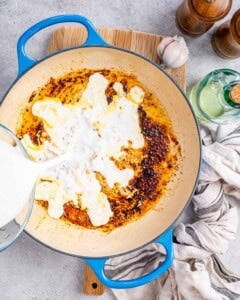 milk being poured over the seared garlic in pan.