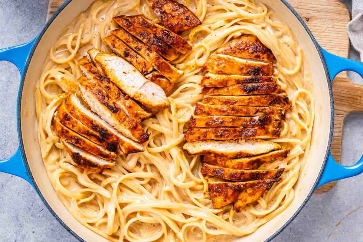 pasta in a skillet topped with two sliced Cajun chicken breasts.