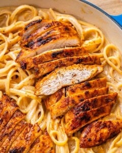 seared sliced cajun chicken over alfredo pasta in skillet.