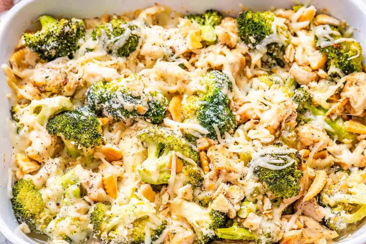chicken divan with veggies in a casserole dish topped with shredded cheese.